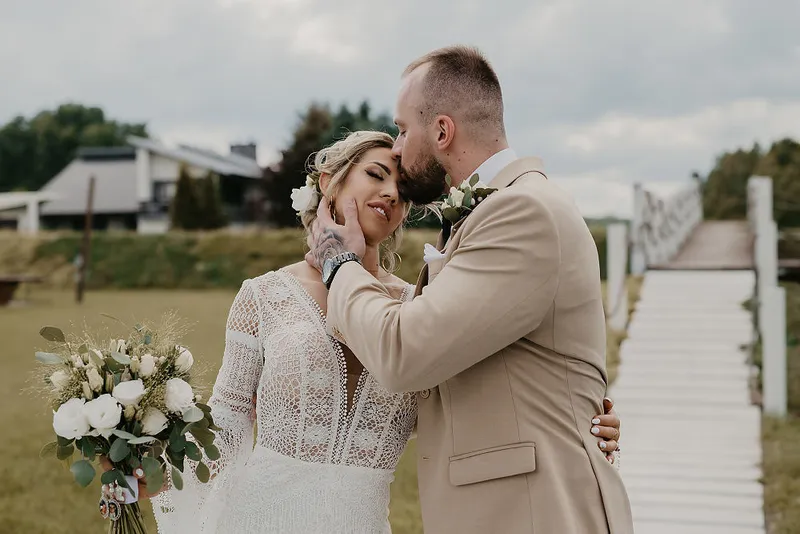 Pan Młody całuje Pannę Młodą podczas plenerowego portretu ślubnego przy pomoście