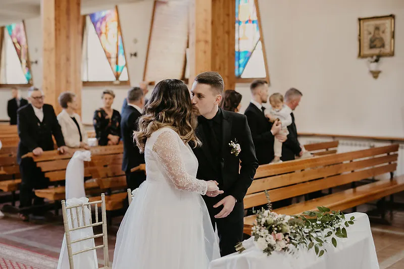 Para Młoda całuje się po ceremonii ślubnej w kościele, a goście stoją w ławkach