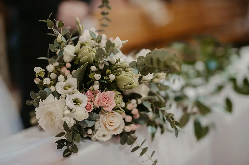 Bukiet ślubny z różami i eukaliptusem ułożony przy ławce w kościele Bukiet ślubny z różami i eukaliptusem ułożony przy ławce w kościele