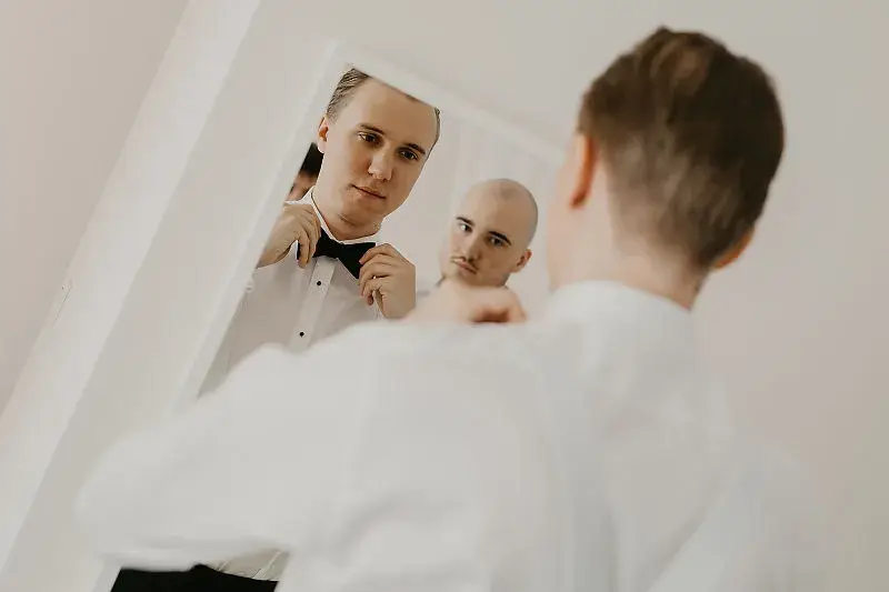 Pan młody poprawia muchę przed lustrem