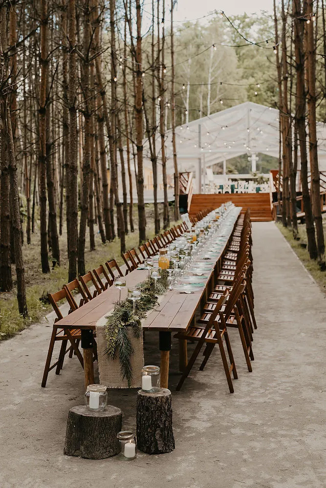 Długi stół weselny ustawiony w leśnej przestrzeni z dekoracjami Długi stół weselny ustawiony w leśnej przestrzeni z dekoracjami