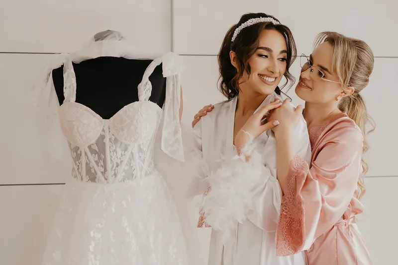 Panna młoda z druhną podczas przygotowań ślubnych obok sukni
