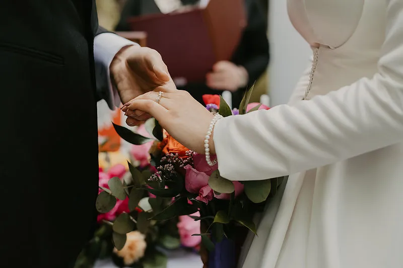Zakładanie obrączki podczas ceremonii ślubnej przy bukiecie kwiatów