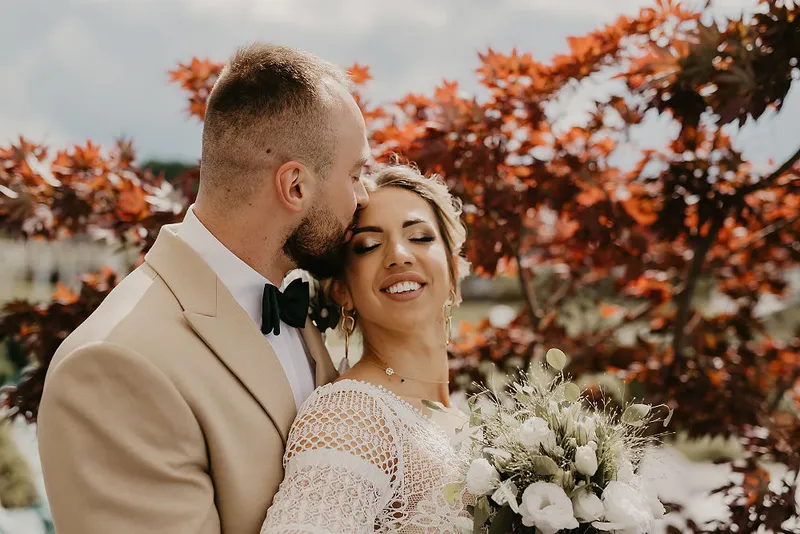 Pan Młody całuje Pannę Młodą w czoło podczas plenerowego portretu ślubnego