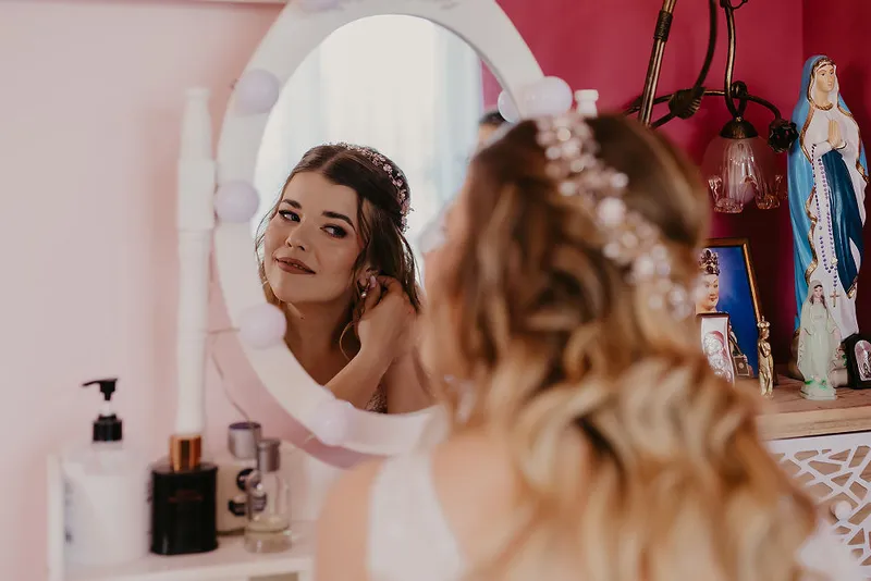 Panna Młoda poprawiająca kolczyk przy lustrze podczas przygotowań do ślubu Panna Młoda poprawiająca kolczyk przy lustrze podczas przygotowań do ślubu