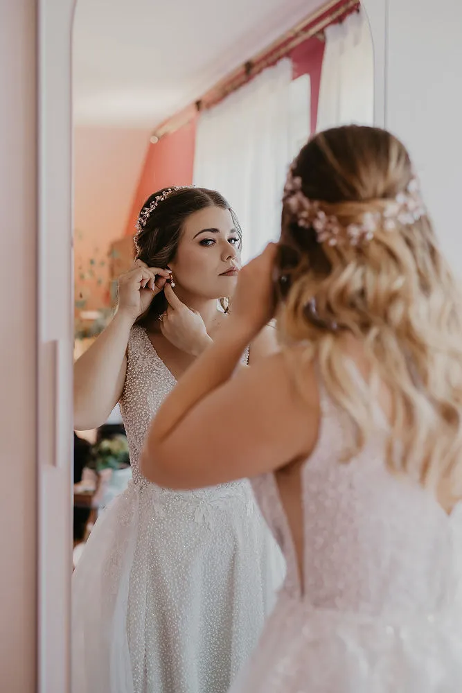 Panna młoda zakłada kolczyk przed lustrem podczas przygotowań do ślubu